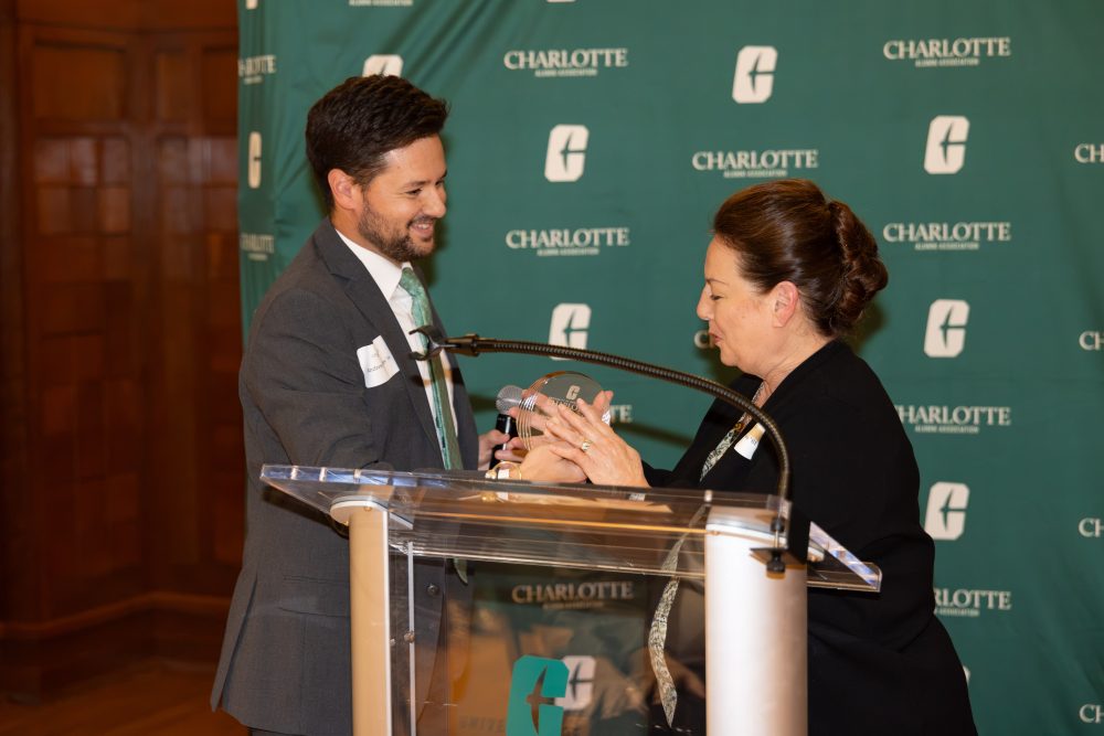 A person in a suit receives an award from another individual at a Charlotte Alumni Association event.